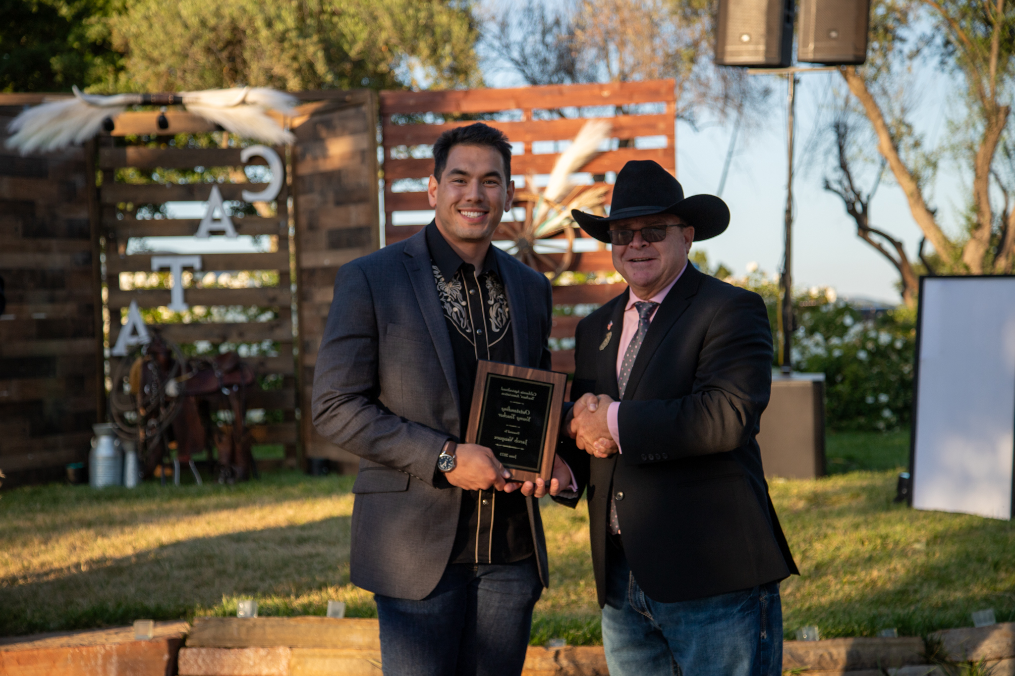 A man in a dark cowboy hat hands a glass trophy to agriculture instructor, Jacob Vasquez.